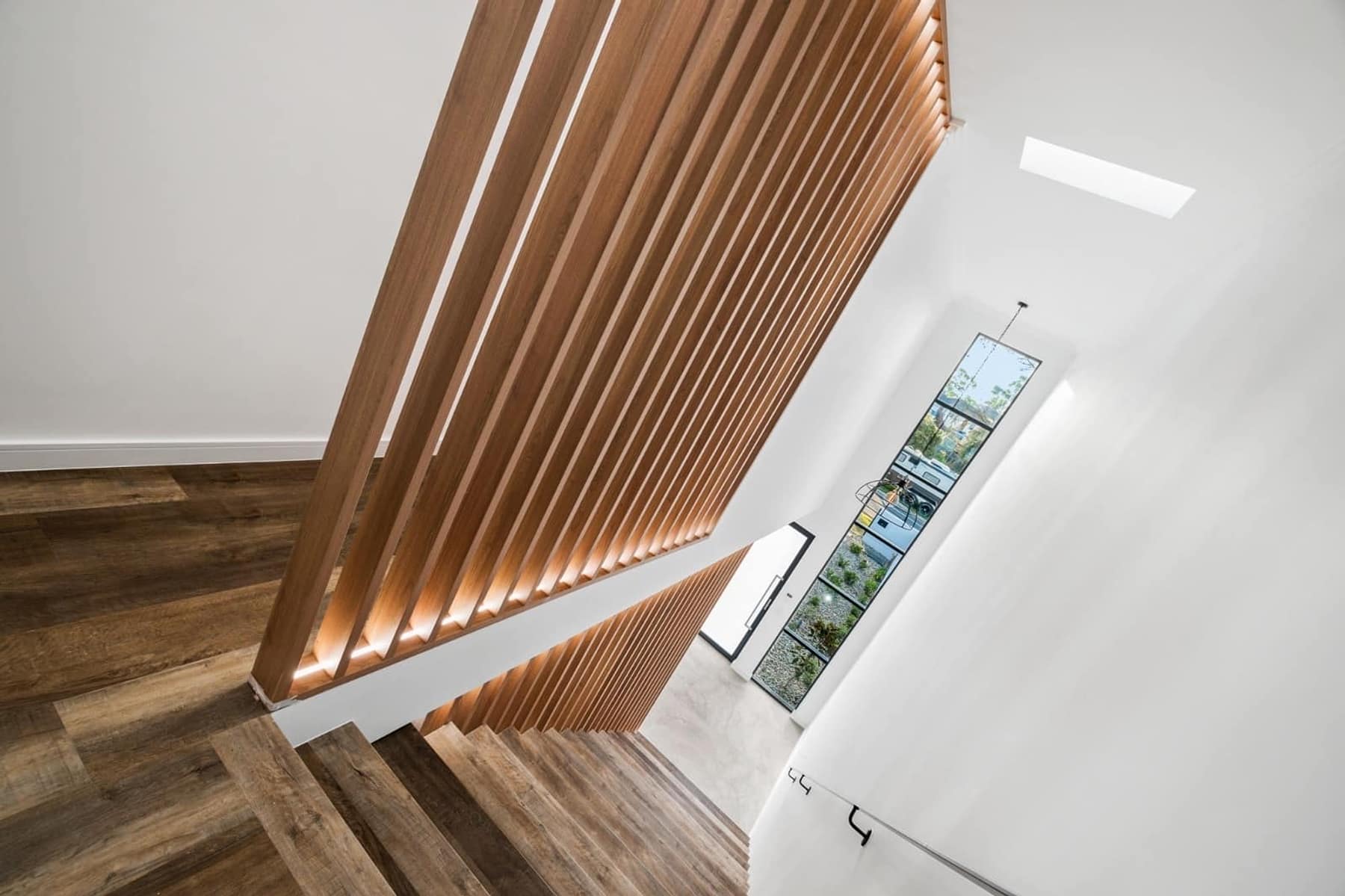 Stair void wrapped in vertical timber battens over herringbone-laid timber floors